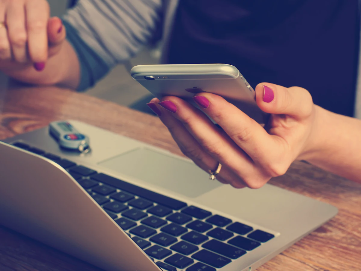 A person using a phone beside a laptop.